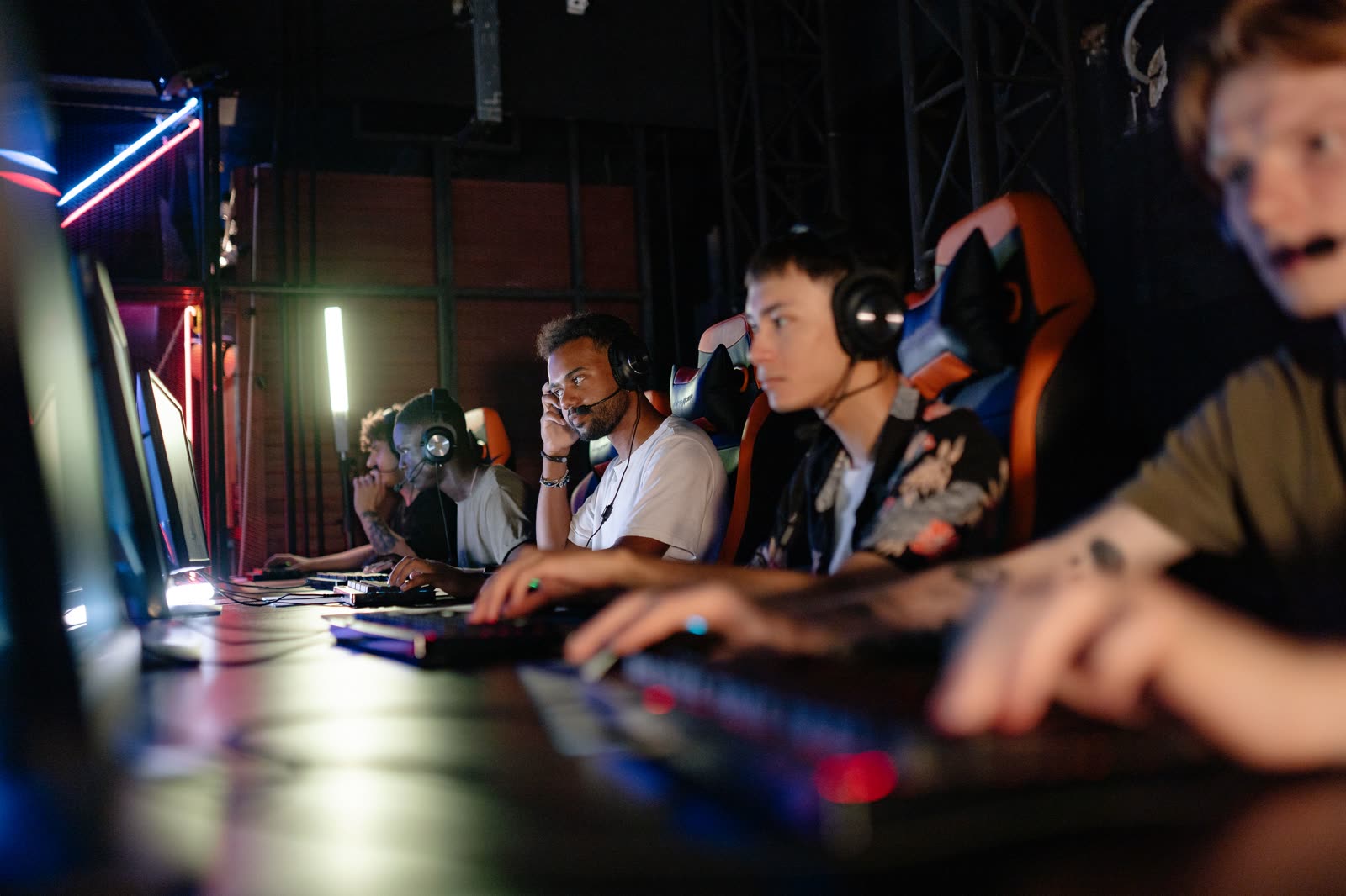 A row of players in gaming chairs at a lit bank of stations along the wall